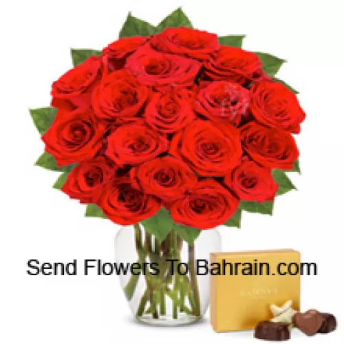 24 roses rouges avec quelques fougères dans un vase en verre accompagnées d'une boîte de chocolats importée