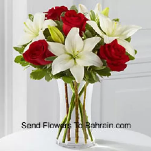 Roses rouges et lys blancs avec quelques remplissages saisonniers dans un vase en verre